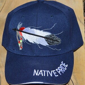 May include: A navy blue baseball cap with an embroidered white feather and arrow design. The words "NATIVE PRIDE" are embroidered in white on the front of the cap.