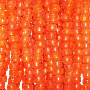 May include: A strand of bright orange glass beads. The beads are small and round, with a slightly irregular shape. They are strung together on a clear thread.