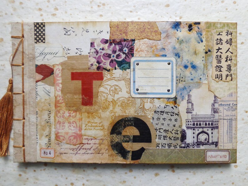 May include: A handmade journal with a brown cover featuring a collage of paper scraps, including a red letter "T", a black letter "e", and a black and white image of a building. The journal has a brown tassel and the text "No. 4" is visible on the cover.