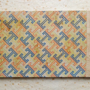 May include: A vintage, hand-bound book with a geometric pattern cover in shades of blue, orange, and yellow. The cover is made of paper and has a decorative binding with a tassel.