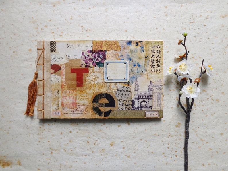 May include: A handmade journal with a brown cover and a colorful collage of paper scraps, stamps, and text. The journal has a brown tassel and is tied with a string. The text on the cover reads "科婦人科專門 請大醫證明 門産人丼".