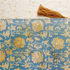 May include: A blue and gold patterned paper with a tassel bookmark. The pattern features stylized flowers and leaves.