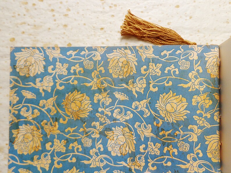 May include: A blue and gold patterned paper with a tassel bookmark. The pattern features stylized flowers and leaves.