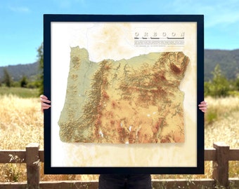 May include: A framed map of Oregon with a topographic relief design. The map is printed on a cream-colored paper with a black frame. The title "OREGON" is printed in black at the top of the map. The map shows the state's major geographic features, including the Cascade Range, the Columbia River, and the Willamette Valley.