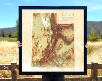 May include: A framed topographic map of Utah with a beige background and brown, green, and red elevation markings. The map is titled "Utah" in black text.