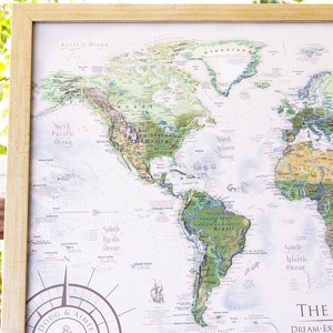 May include: A framed world map with a white background and green and brown continents. The map is titled "The World" and has the text "Dream-Explore-Discover" below the title. The map also includes a compass rose in the bottom left corner.