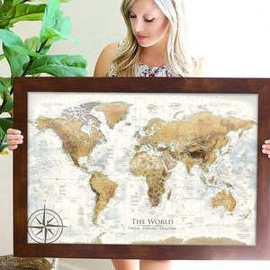 Puede incluir: Un mapa del mundo enmarcado con fondo marr&oacute;n y una br&uacute;jula en la esquina inferior izquierda. El mapa est&aacute; titulado "The World: Dream. Explore. Discover."