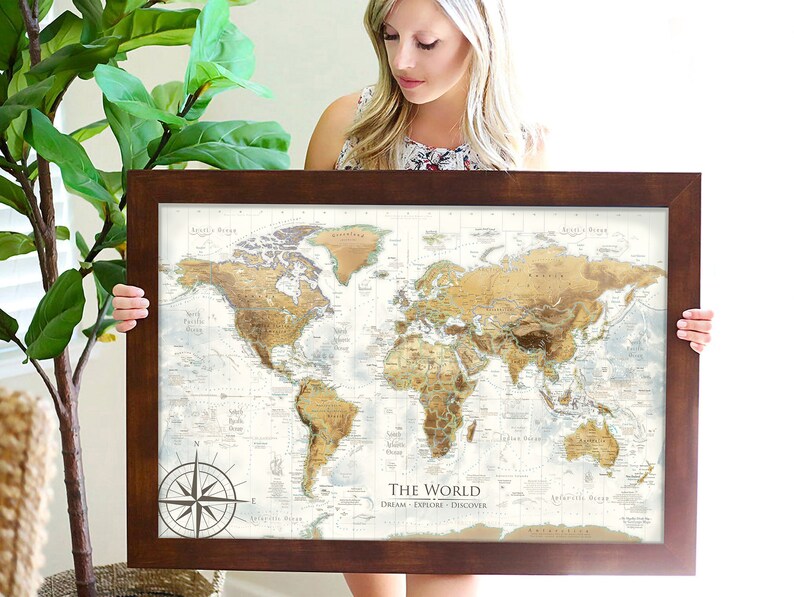 Puede incluir: Un mapa del mundo enmarcado con fondo marr&oacute;n y una br&uacute;jula en la esquina inferior izquierda. El mapa est&aacute; titulado "The World: Dream. Explore. Discover."