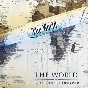 May include: A rolled up world map with a vintage style design. The map is printed on a light blue background with brown and black lines and text. The map is titled "The World" and has the words "Dream Explore Discover" printed below the title.