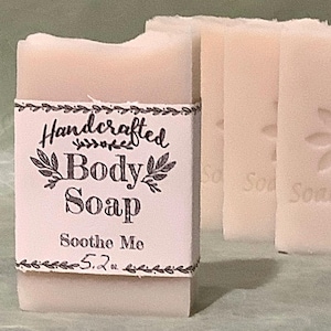 May include: Three bars of handcrafted body soap with a white label that reads "Handcrafted Body Soap Soothe Me 5.2 oz".