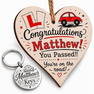 May include: A heart-shaped wooden hanging plaque with a red car graphic, a torn L-plate, and text reading Congratulations Matthew! You Passed!! You're on the road! paired with a round silver metal keychain engraved with a car and Matthew's Keys.