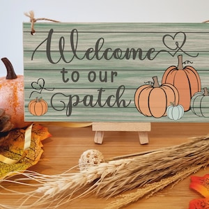 May include: Welcome to our patch sign with a rustic woodgrain background and a green and white colour scheme. The sign features a heart and several pumpkins in orange and green.