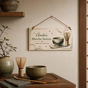 May include: A rectangular hanging sign with a rope, featuring the text Amelia's Matcha Station and a quiet cup, a calm mind. The sign displays illustrations of a green matcha bowl, a bamboo whisk, and a bamboo scoop on a light background.
