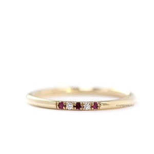 May include: A delicate gold band ring with a row of alternating ruby and diamond stones. The ring is set on a white background. KHIMIJWELRY is printed on the right side of the image.
