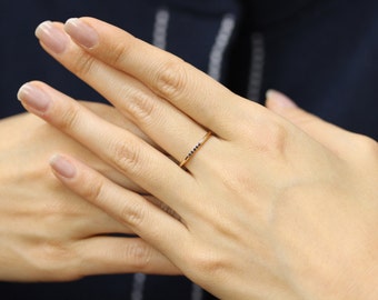 May include: A thin gold band ring with a row of small black diamonds.