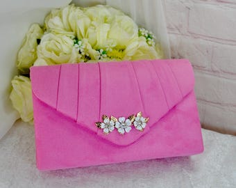 Op de afbeelding: Een roze suède clutch met een gouden en witte bloemenversiering.