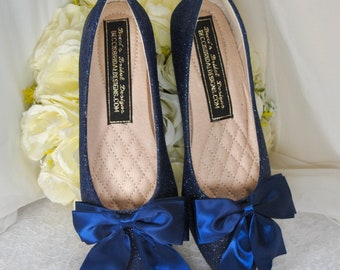Op de afbeelding: Een paar donkerblauwe glitter ballerina's met een satijnen blauwe strik op elke schoen. De schoenen hebben een spitse neus en zijn gelabeld "Becca's Bridal Designs, BECCASBRIDALDESIGNS.COM".