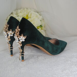 May include: A pair of dark green velvet high heels with gold and white floral embellishments on the heel.