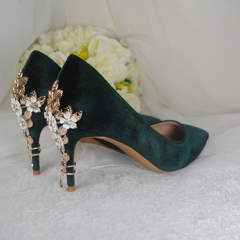 May include: A pair of dark green velvet high heels with gold and white floral embellishments on the heel.