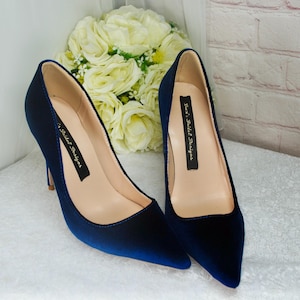 May include: A pair of navy blue velvet pointed-toe heels with a stiletto heel. The shoes have a label on the inside that reads "Kaci's Bridal Designs".