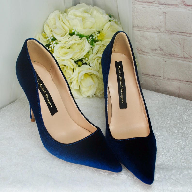 May include: A pair of navy blue velvet pointed-toe heels with a stiletto heel. The shoes have a label on the inside that reads "Kaci's Bridal Designs".