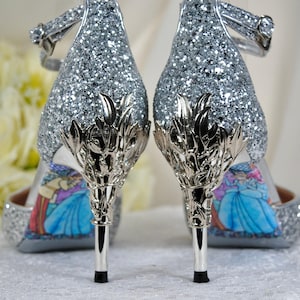 May include: A pair of silver glitter high heel shoes with a silver metal design on the heel. The shoes have a blue and purple print on the sole.