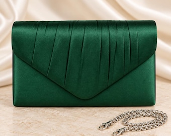 Puede incluir: Un bolso de mano tipo sobre en satén verde esmeralda oscuro con un diseño de solapa plisada y cierre en forma de V. Este bolso de noche rectangular incluye una correa de cadena metálica plateada extraíble con mosquetones en los extremos.