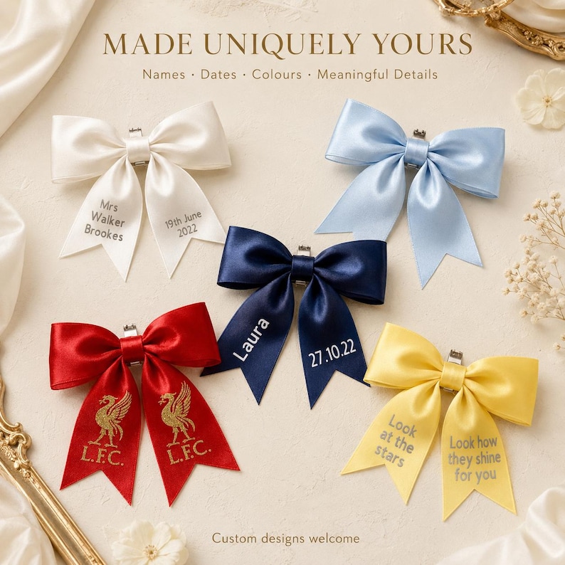 May include: Five satin hair bows in white, light blue, navy blue, red, and yellow. The white bow features text Mrs Walker Brookes and 19th June 2022. The navy bow features Laura and 27.10.22. The red bow features gold L.F.C. logos. The yellow bow features text.