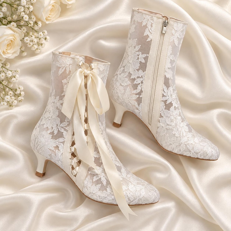 May include: A pair of white lace ankle boots featuring a floral pattern, a kitten heel, and a front ribbon lace-up closure. One boot displays a decorative satin ribbon tied in a bow, while the other shows a side zipper closure detail.