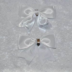 May include: Two white satin bows with personalized text. The top bow has the text "Mrs Manning" and "27th October 2021". The bottom bow has the text "Welcome Home" and "Baby Birmingham".