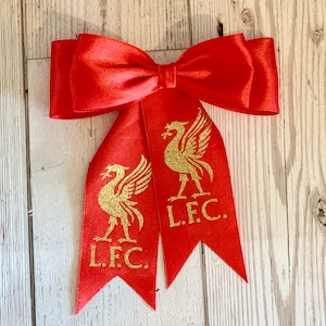 May include: Red satin bow with two gold glitter Liverpool FC crests and the text "L.F.C."