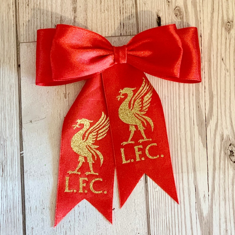 May include: Red satin bow with two gold glitter Liverpool FC crests and the text "L.F.C."