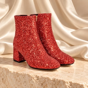 Puede incluir: Un par de botines cubiertos de purpurina roja vibrante. Estos botines cuentan con una punta redondeada, un tac&oacute;n de bloque y un cierre de cremallera lateral. La superficie exterior est&aacute; totalmente texturizada con finos destellos rojos brillantes.