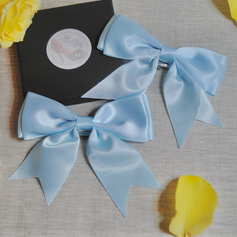 May include: Two light blue satin hair bows with a clip on the back. The bows are tied in a classic bow shape with two tails.