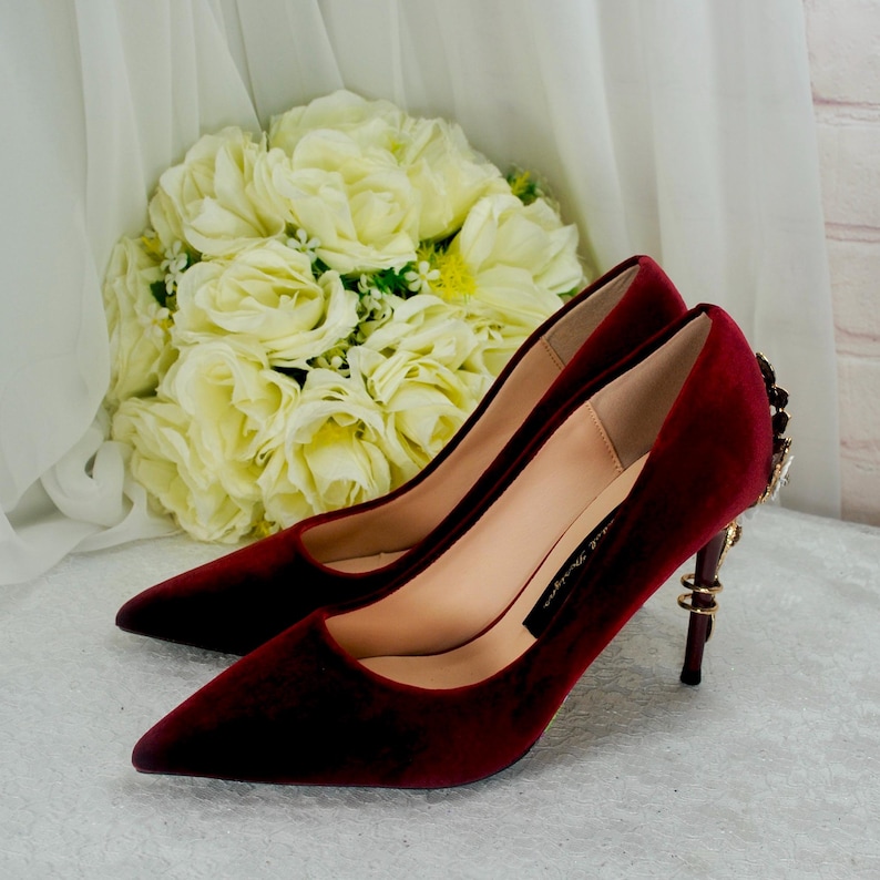 May include: A pair of burgundy velvet high heels with a pointed toe and a gold embellished heel.