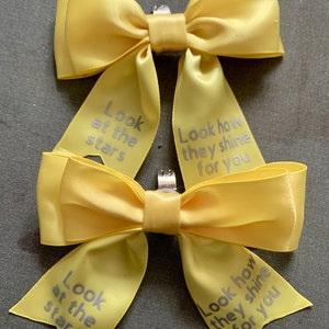 May include: Two yellow satin bows with silver text. The text on the bows reads "Look at the stars" and "Look how they shine for you".