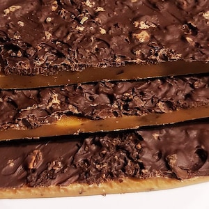 May include: A close-up of a stack of chocolate toffee with a caramel centre. The toffee is covered in a layer of dark chocolate and has a slightly crunchy texture.