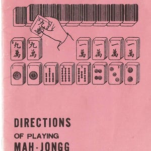 May include: Pink cover with black illustrations and text for the game Mah-Jongg. The image shows a hand holding a tile, along with other tiles and the words "Directions of Playing Mah-Jongg". The text also includes "Chinese Game of Four Winds".