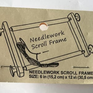 May include: A tan card featuring a black illustration of a needlework scroll frame. The text "Needlework Scroll Frame" is above the frame. The size is 15.2 cm x 30.5 cm.