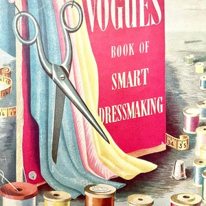 以下が含まれることがあります： ヴォーグのスマートドレスメイキングの本のヴィンテージイラスト。表紙は赤で、白い文字が書かれています。糸巻き、指ぬき、はさみ、生地見本があります。