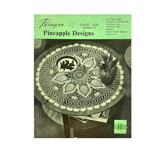 Op de afbeelding: Een vintage haakpatroonboekomslag met een gehaakt ananas-ontwerp doily op een tafel. De omslag is groen en heeft de tekst "Paragon Crochet Book Number 110 Pineapple Designs" en "Price 35 Cents".