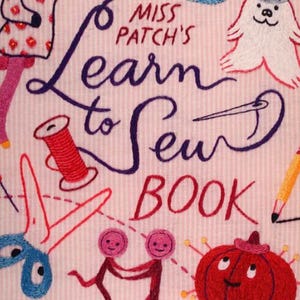May include: A pink book with the title "Miss Patch's Learn to Sew Book" embroidered in purple and red thread. The book cover is decorated with various sewing-related items, including a spool of thread, a needle, scissors, a thimble, and a button.