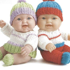 May include: Two baby dolls in knitted outfits. One doll wears a white sweater with purple and green stripes, a green skirt, and a matching hat. The other doll has a white sweater with red stripes, red trousers, a blue hat, and blue shoes.