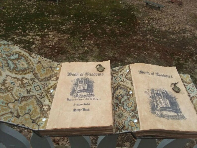 Pu&ograve; includere: Due libri aperti intitolati "Book of Shadows" con un'estetica vintage. Le copertine presentano un lucchetto e un'illustrazione dettagliata. Le pagine sono invecchiate e il libro &egrave; rilegato con un tessuto fantasia nei toni del marrone, blu e crema.