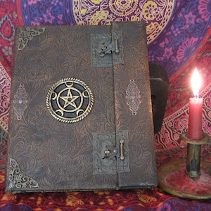 May include: A brown leather-bound journal with ornate metal accents, including a pentagram and moon phases design. The journal is closed and sitting on a colorful patterned fabric.