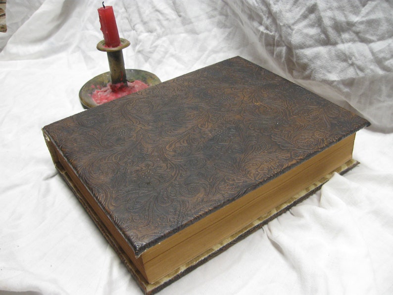 Puede incluir: Un libro encuadernado en cuero marr&oacute;n con un patr&oacute;n decorativo en relieve en la portada. El libro est&aacute; cerrado y se encuentra sobre una superficie blanca.