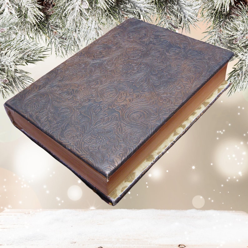 Puede incluir: Un libro encuadernado en cuero marr&oacute;n con un patr&oacute;n decorativo en relieve. El libro est&aacute; cerrado y sobre una superficie blanca.