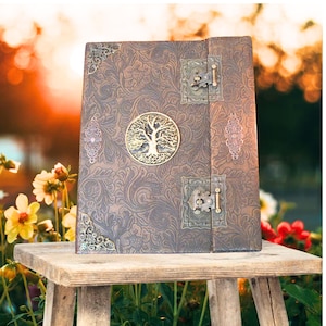 May include: A brown leather journal with a tree of life design and metal accents. The journal has a lock and key.