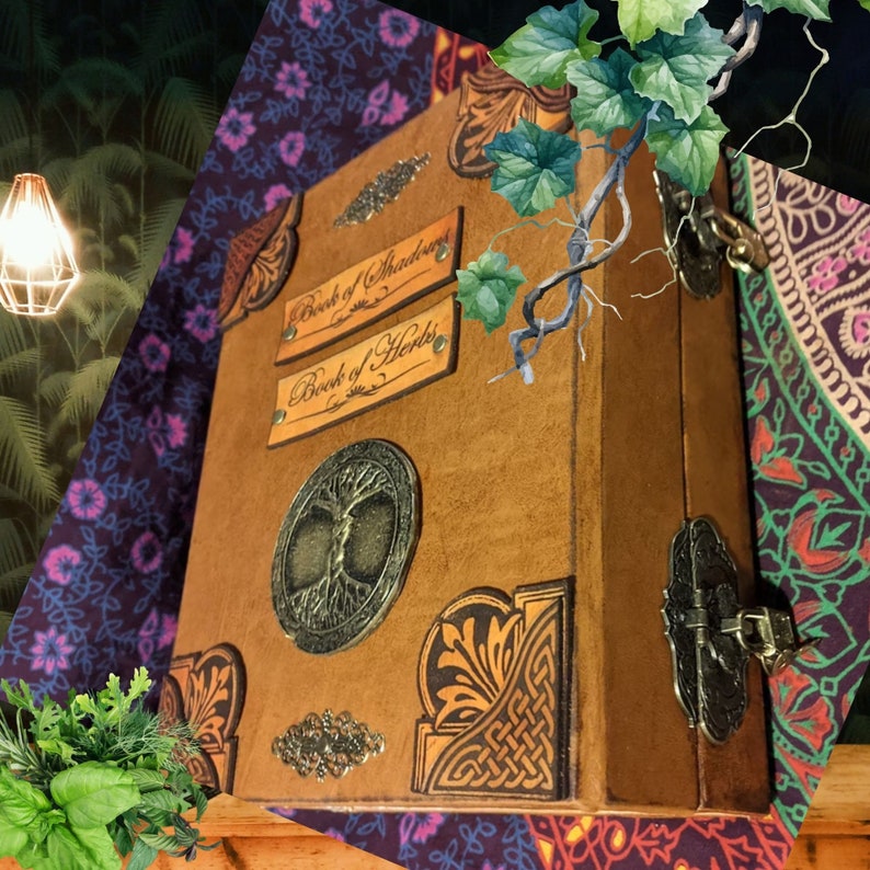 Pu&ograve; includere: Un libro rilegato in pelle marrone con dettagli e chiusure in metallo. Il libro riporta le scritte "Book of Shadows" e "Book of Herbs" sulla copertina. Un emblema dell'albero della vita &egrave; presente sul davanti. I disegni decorativi degli angoli e gli abbellimenti metallici aggiungono dettagli.