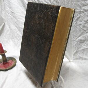 Puede incluir: Un libro encuadernado en cuero marr&oacute;n oscuro con un patr&oacute;n decorativo en relieve. El libro tiene un lomo grueso y est&aacute; cerrado.